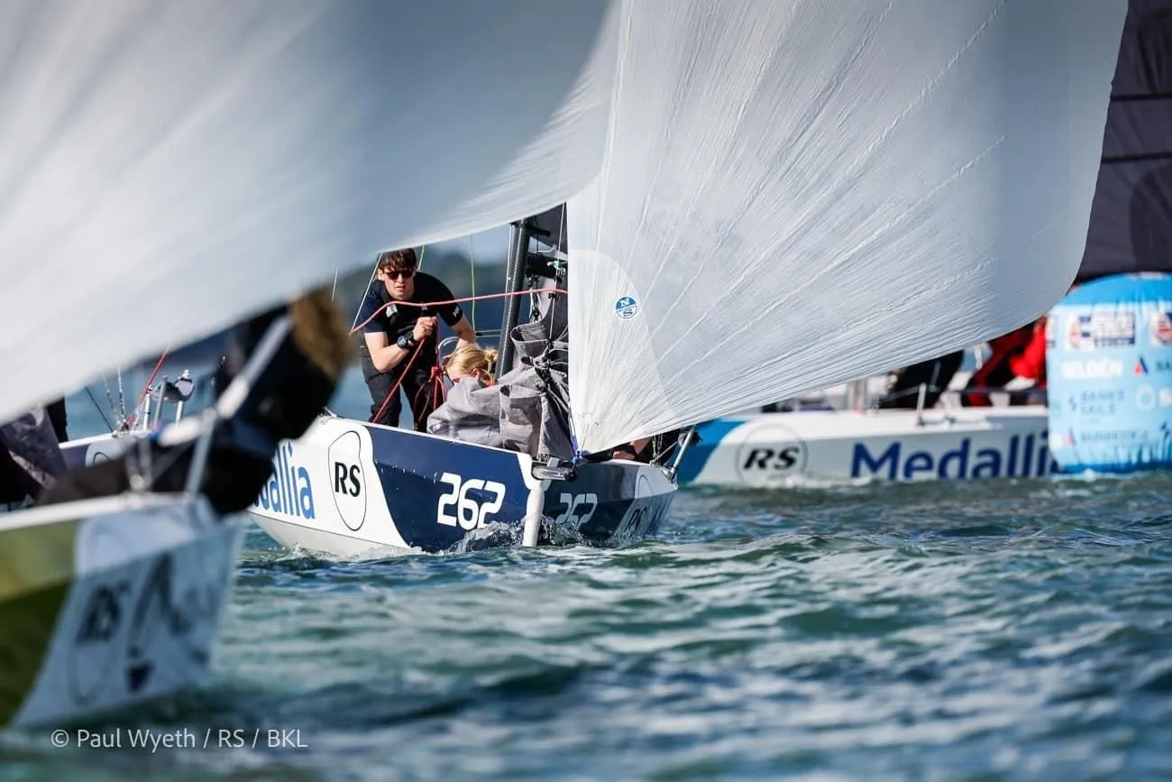 Close-up of sailboats competing in a race on a sunny day, with crew members focused amidst billowing sails.